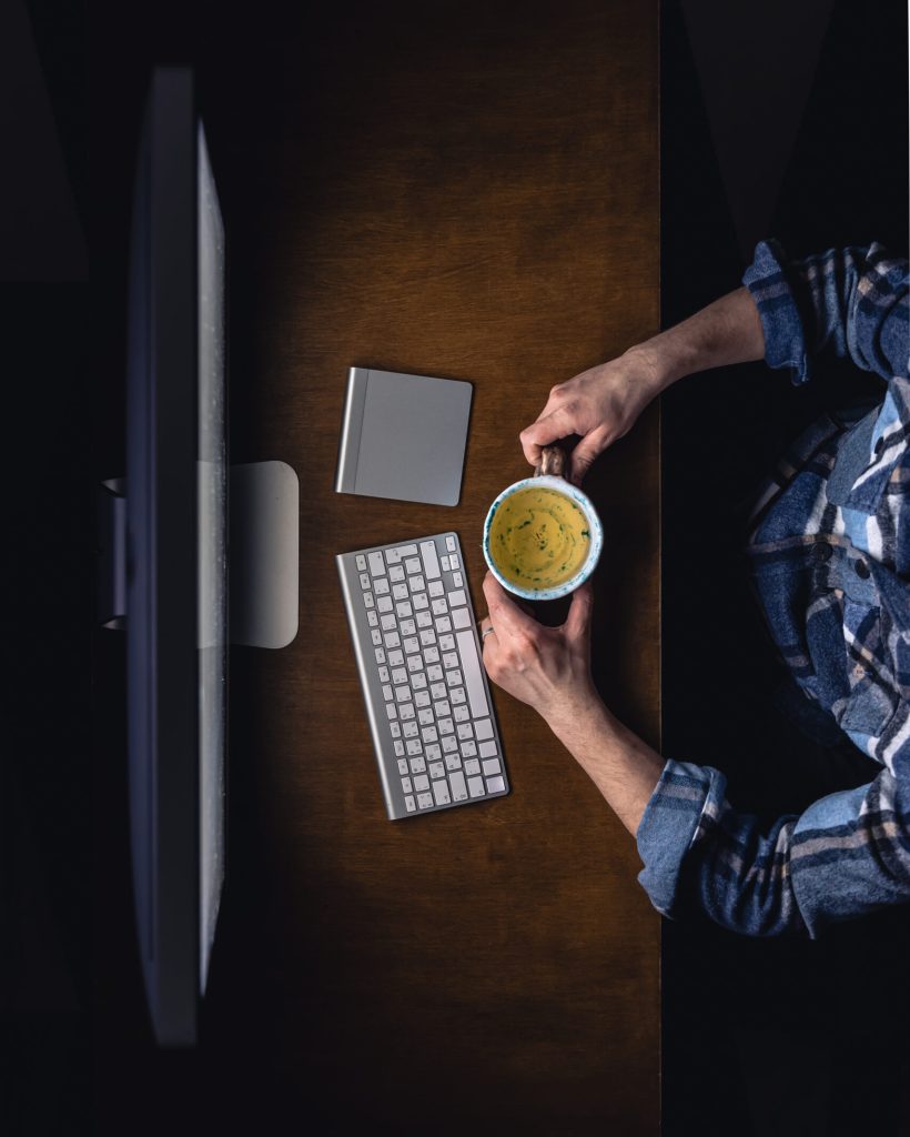 Top view of man working on computer at night, holding mug of tea. Home workspace, work from home at night. Freelance concept.